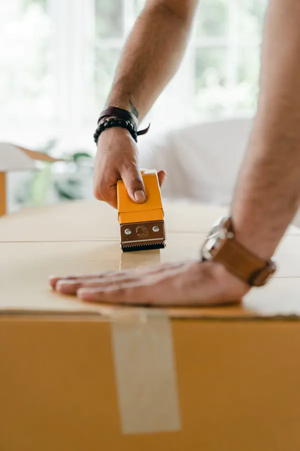 Hands sealing a shipping carton with packing tape